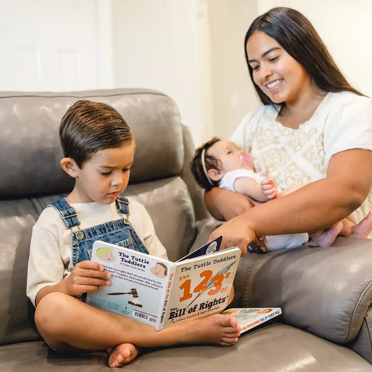 Children's '123 of the Bill of Rights' book held by toddler and parent on sofa