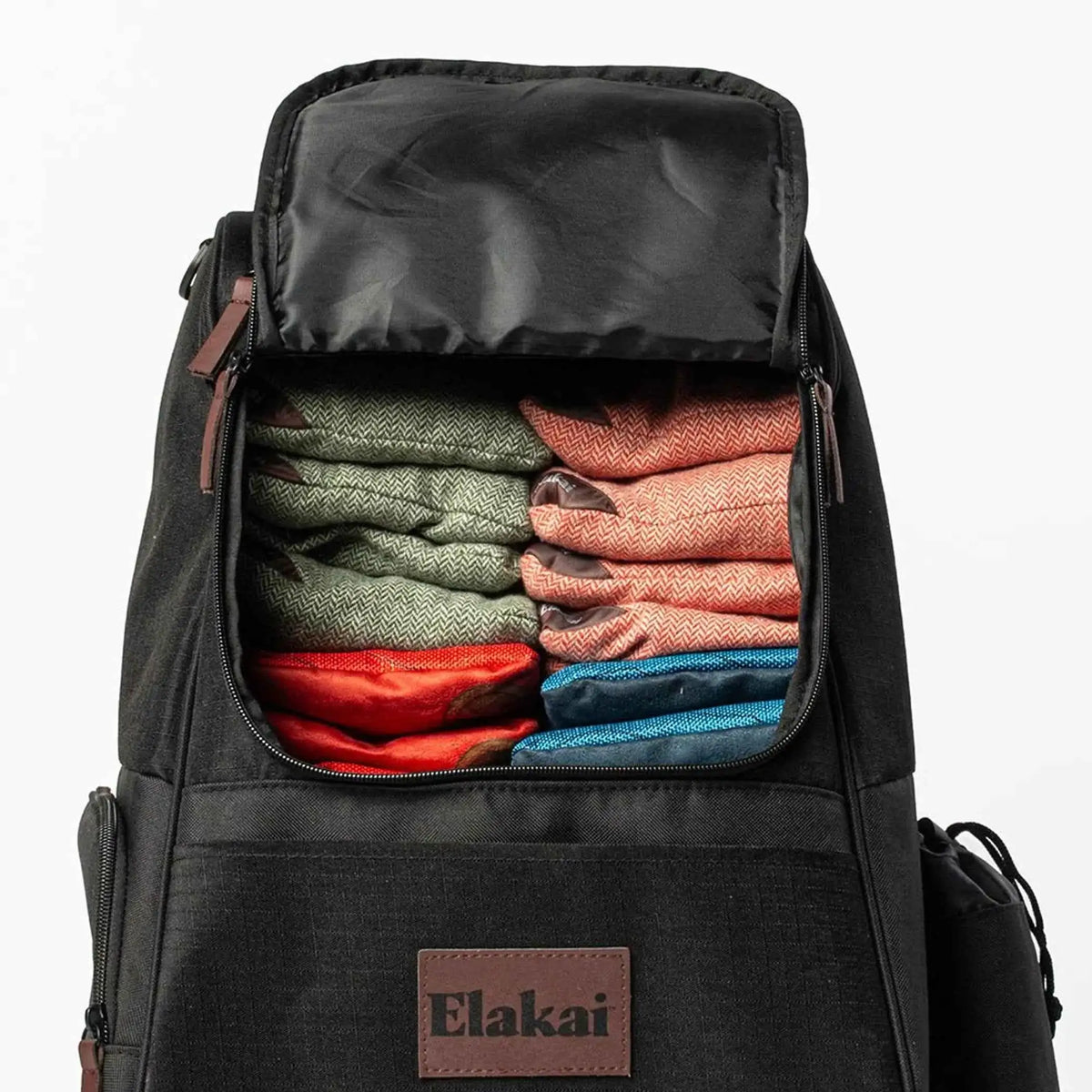 Black backpack open top showing folded multicolor clothes; Elakai logo patch.