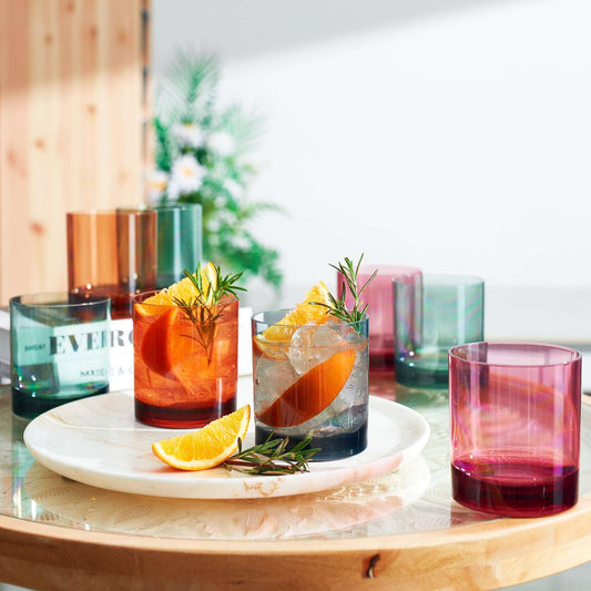 Acrylic lowball tumblers with rosemary garnish in tinted cups, orange, blue, pink