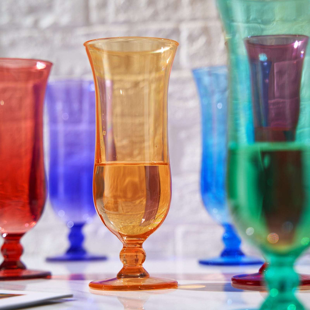 Amber acrylic hurricane glass with stem base, surrounded by colored glasses