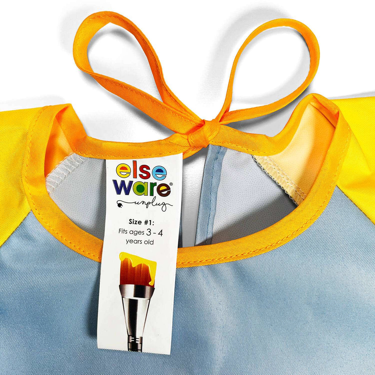 Art smock neckline close-up with orange ties and elseware size label, light blue and yellow