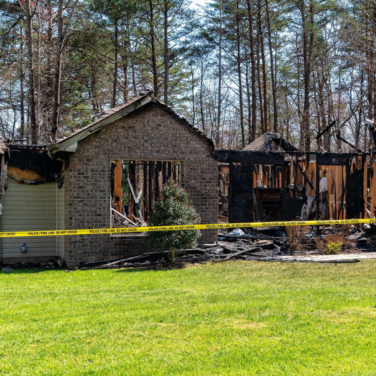 Fire-damaged building with yellow caution tape in an outdoor yard