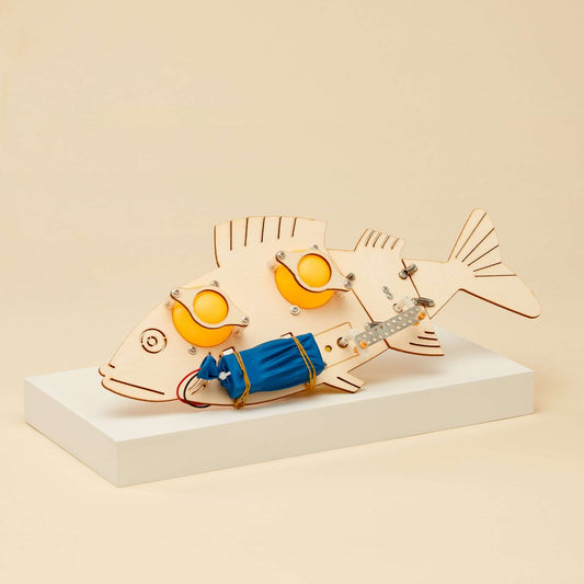 Assembled wooden fish robot with orange eyes, blue band, and tail fins