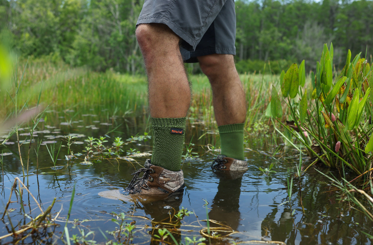 Green ribbed waterproof breathable socks in shallow water, boots splashing
