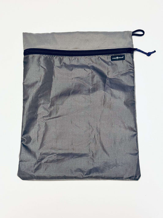 Gray stuff sack pillow with dark zipper and open mesh front.