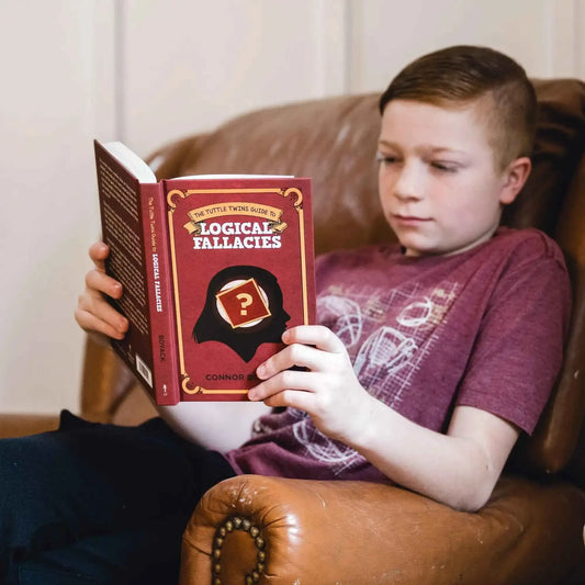 Child reading Logical Fallacies book on couch, holding front cover