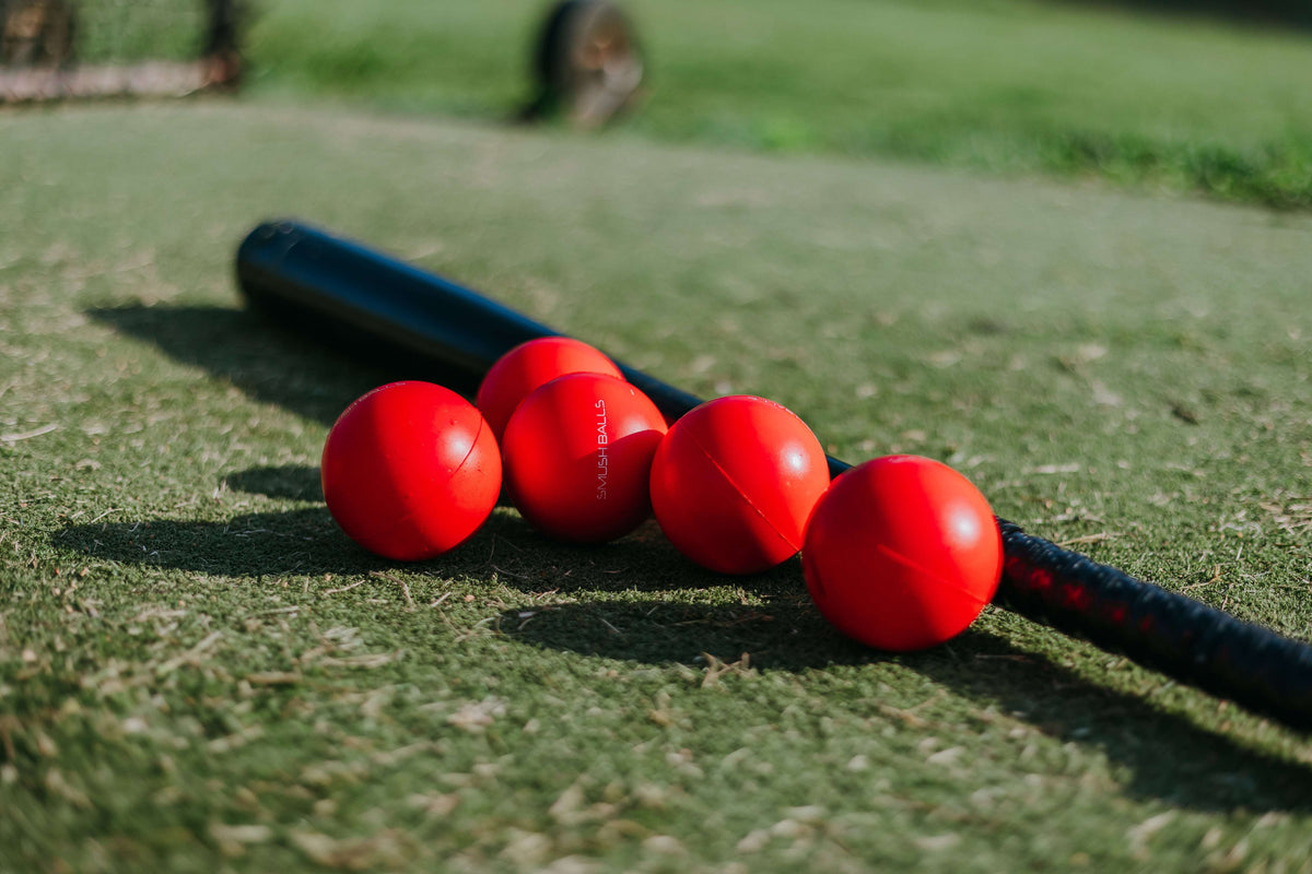 Red Smushballs training baseballs, set of red foam balls clustered on grass with bat handle