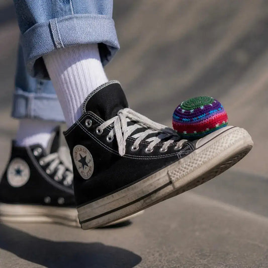 Crocheted footbag with multicolor stripes near a black sneaker