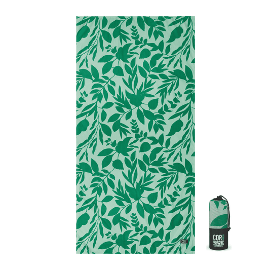 Quick-dry travel towel with bright teal leaf print, small COR label at bottom right