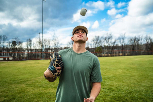 White baseball with red stitching above a pitching glove and player in green