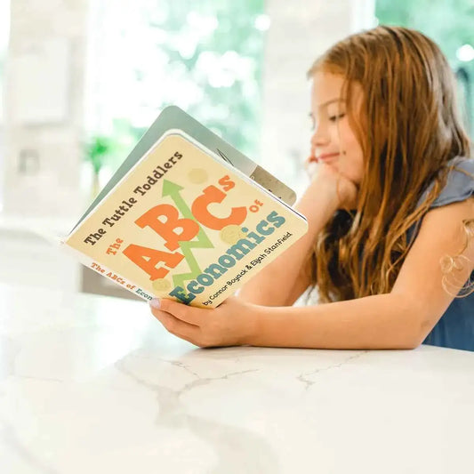 Toddler reading The Tuttle Toddlers ABCs of Economics book with colorful cover
