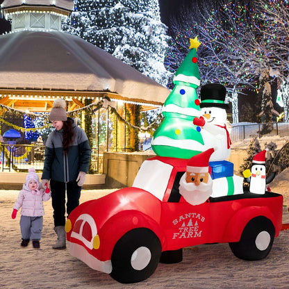 Inflatable red Christmas pickup with Santa, tree, snowman and penguin figures, shown beside people.