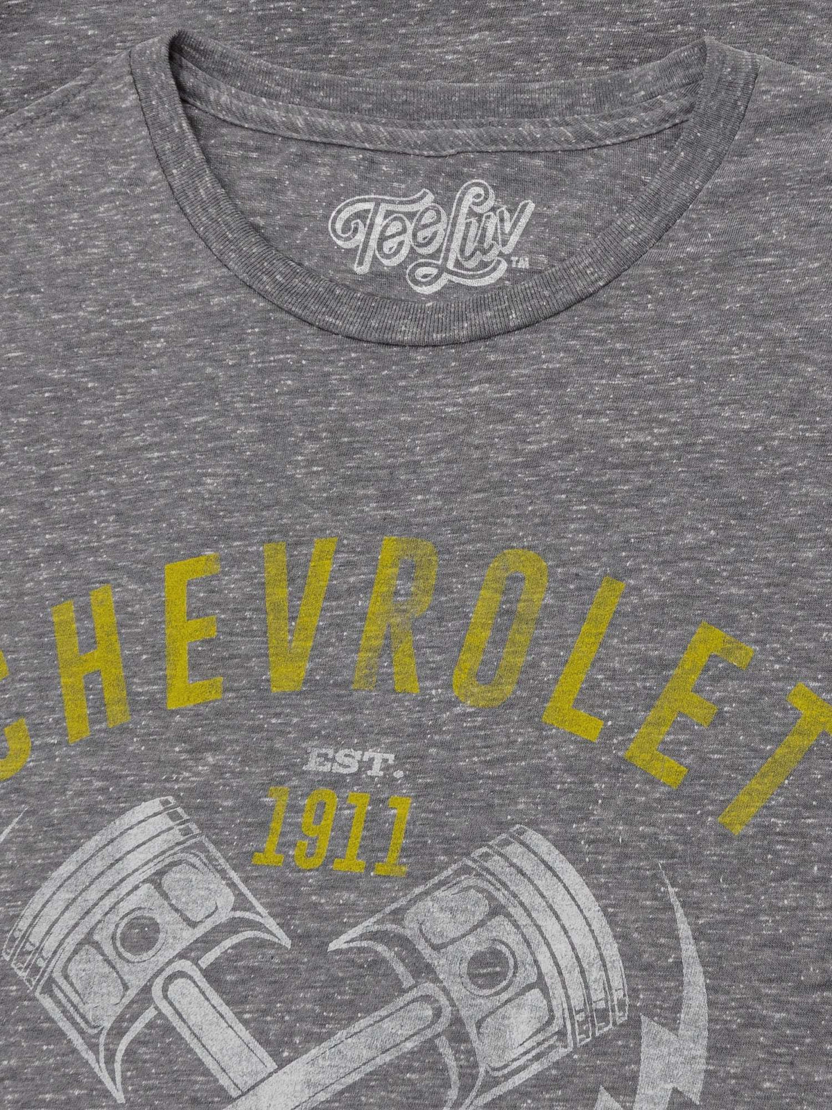 Gray T-shirt neckline with white Tee Luv logo and yellow Chevrolet graphic text