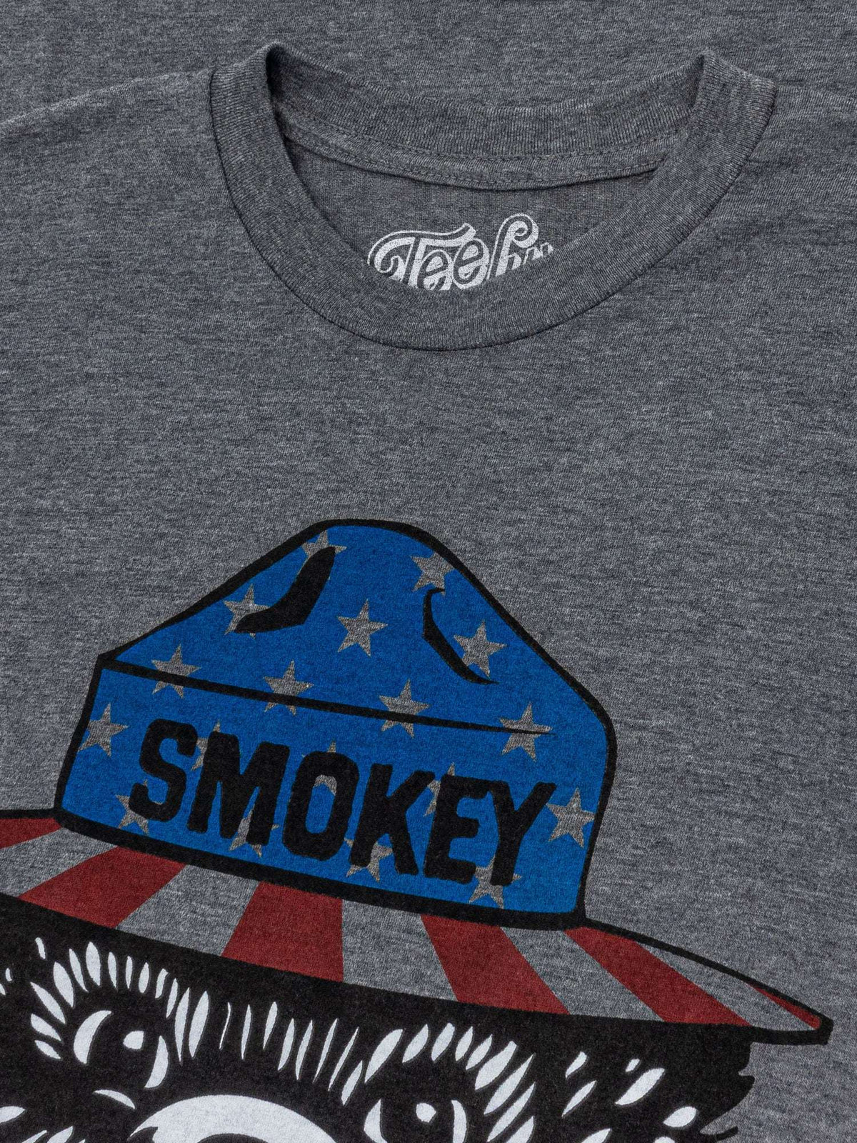 Gray t-shirt close-up of Smokey bear patriotic hat and stars graphic.
