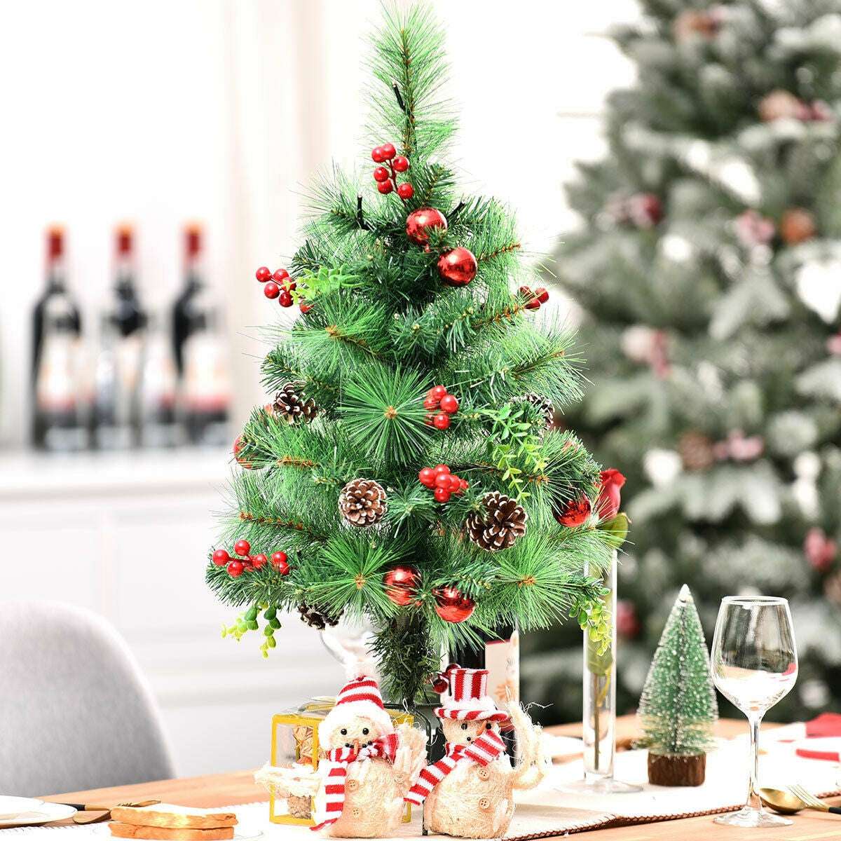 Pre-lit Christmas tree decorated with red berries, ornaments, and pine cones on a tabletop