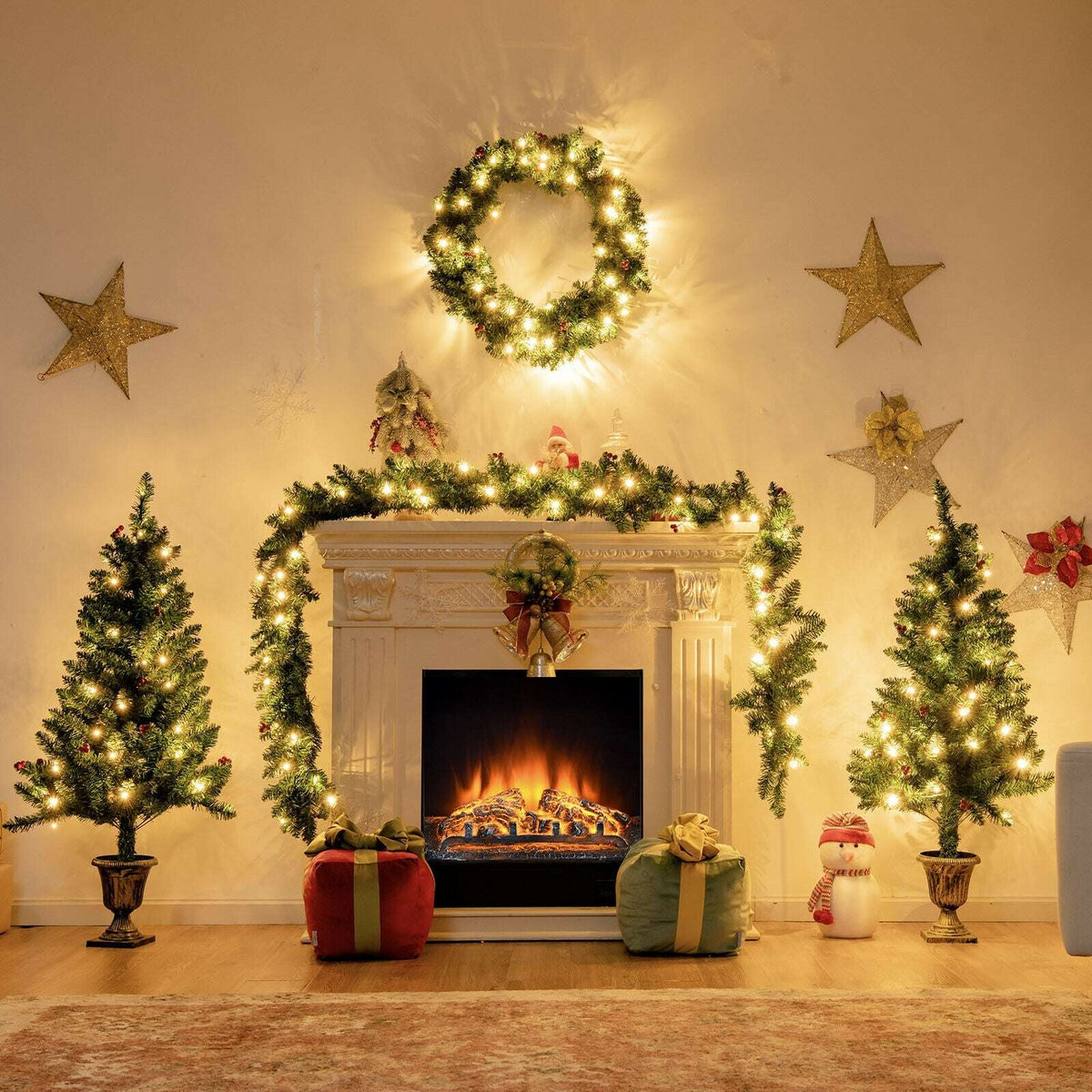 Pre-lit Christmas decor set arranged around a fireplace with trees, wreath, and garland