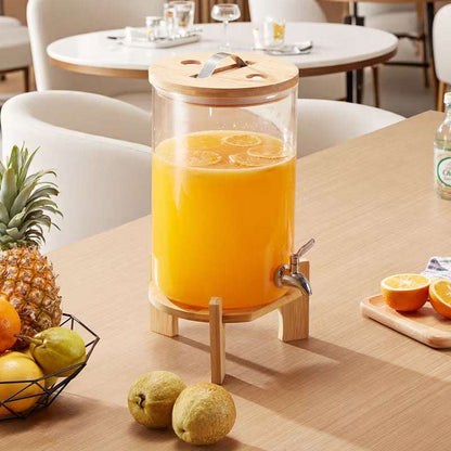Clear glass beverage dispenser with bamboo stand, metal spigot, filled with orange juice