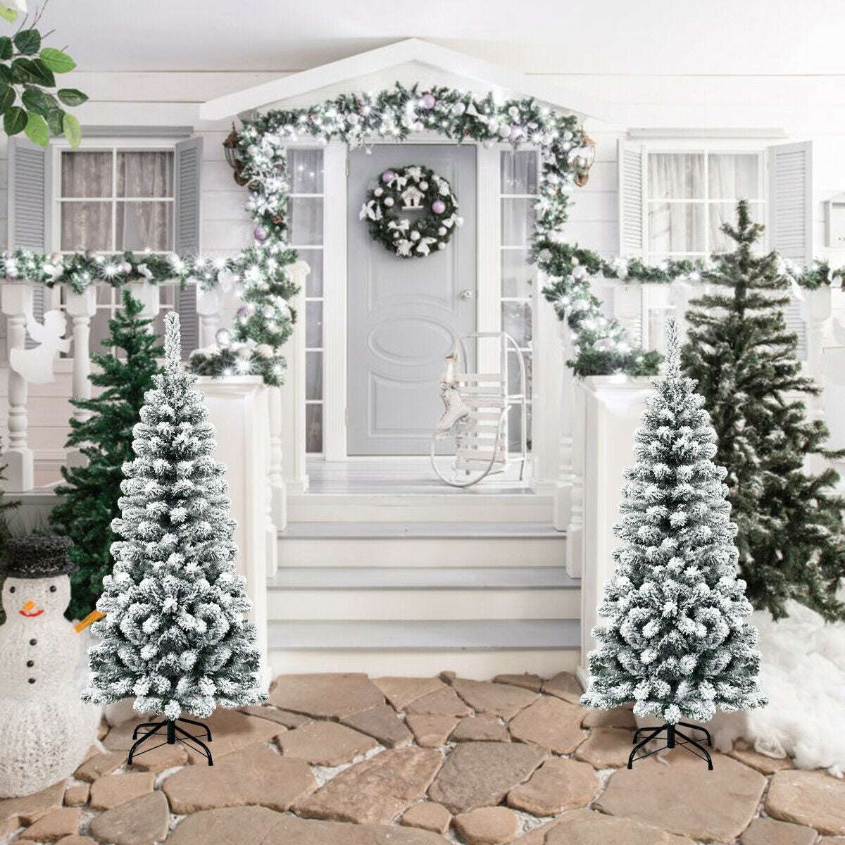 Two snow-flocked pencil Christmas trees with black metal stands