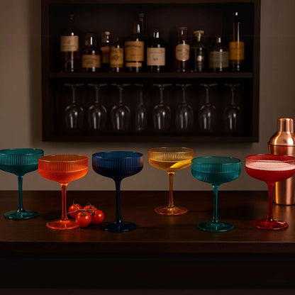 Assorted ribbed coupe acrylic glasses with dark teal, blue, orange, and red tones on a bar shelf