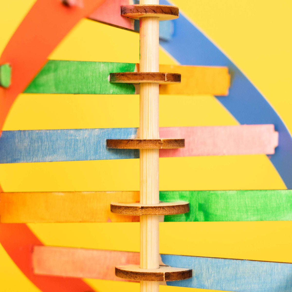 Close-up of vertical wooden rods connecting colorful DNA slats
