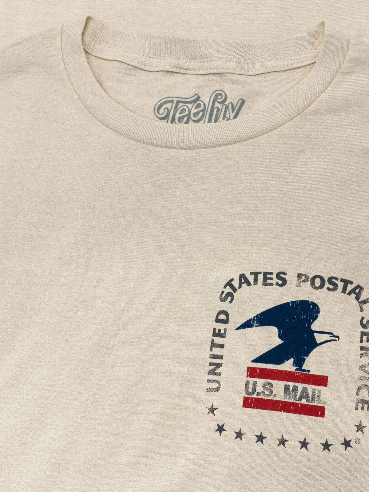 Cream crewneck T-shirt with tealiv logo on collar and partial USPS eagle graphic.