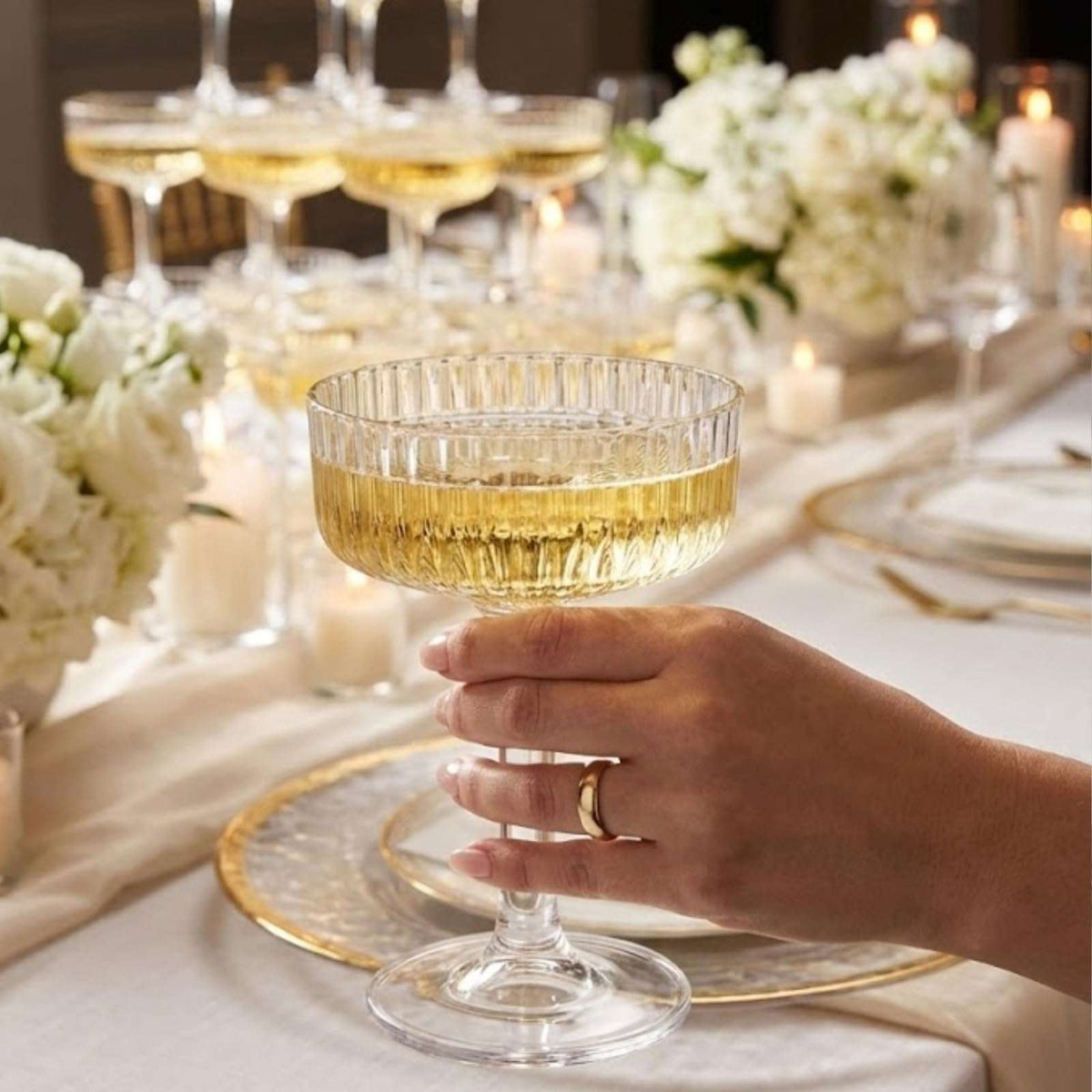 Hand holding a single clear acrylic champagne coupe glass with gold drink
