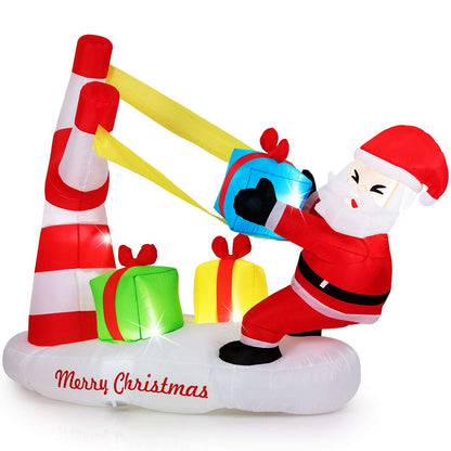 Inflatable Santa braces a blue slingshot beside two gift boxes and a striped base