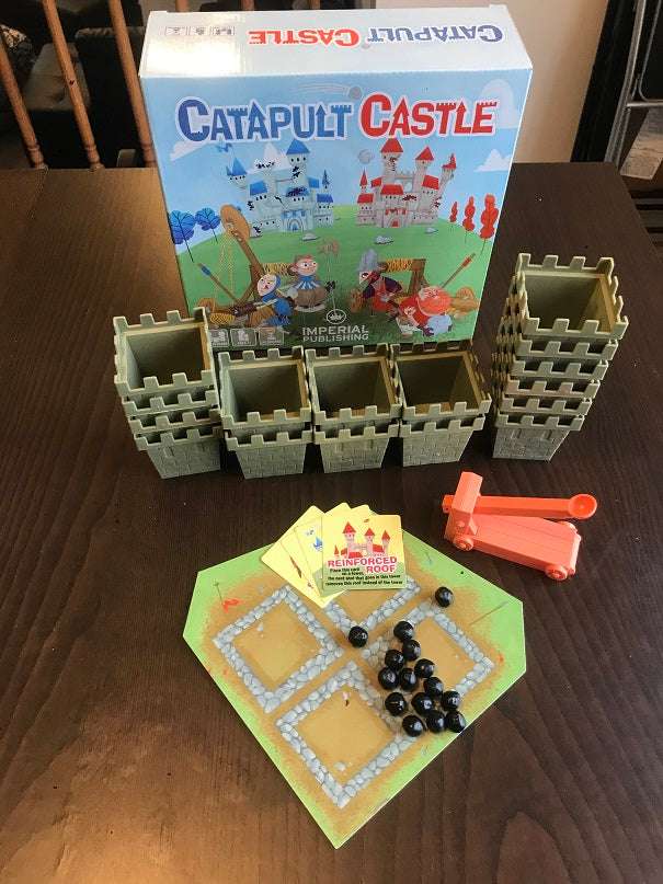 Catapult Castle board game components on table: castle towers, rulebook, catapult and ammo