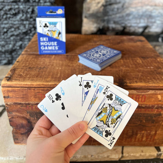 Hand holding playing cards with a king, blue deck box on a wooden table.