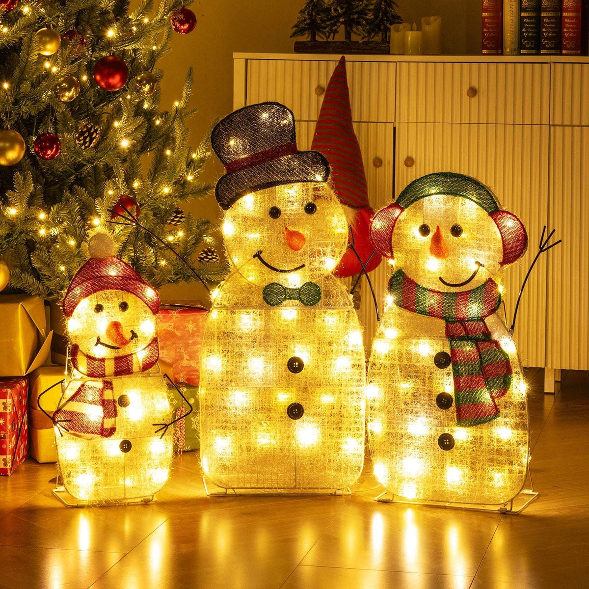 Three illuminated snowmen in a family set, wearing festive hats and red, green and striped accessories