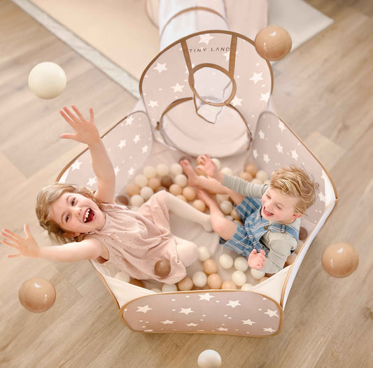 Kids playing in a neutral star-pattern ball pit tent filled with tan and white balls.