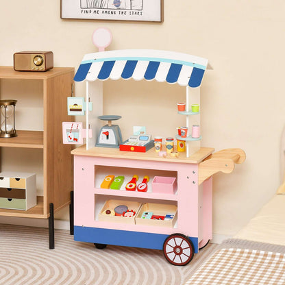 Pink wooden toy market cart with blue and white canopy, shelves, play food, scale and cash register