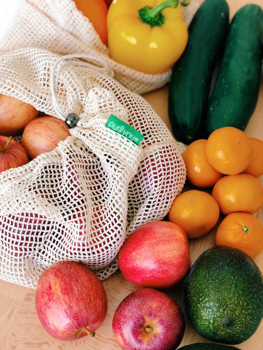 White reusable organic cotton mesh produce bag with drawstring, holding assorted fruits