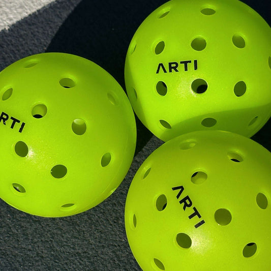 Set of neon green pickleball balls with multiple holes and ARTI branding