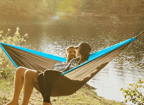 Nylon hammock with blue top and brown underside, used by two people relaxing outdoors