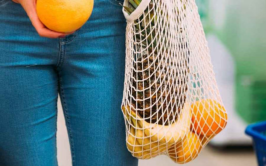 Cream mesh shopping bag with handles, holding oranges