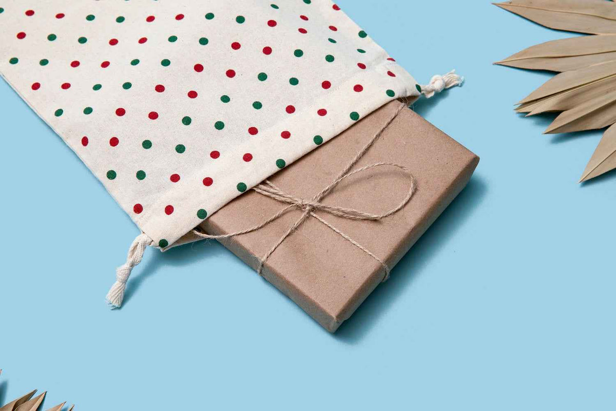 Cotton pouch with red and green dot print, drawstring tassel tied over kraft box