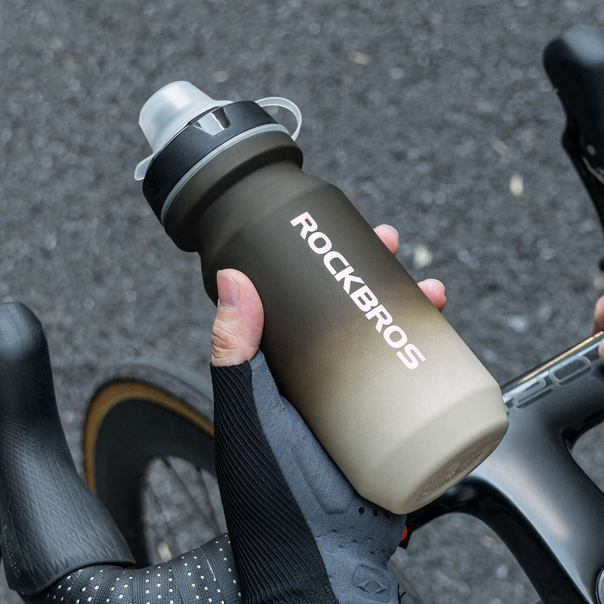 Dark gray bike water bottle with spout lid and strap, mounted on a handlebar