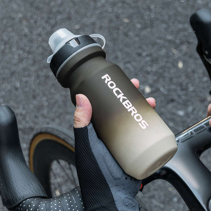 Dark gray bike water bottle with spout lid and strap, mounted on a handlebar