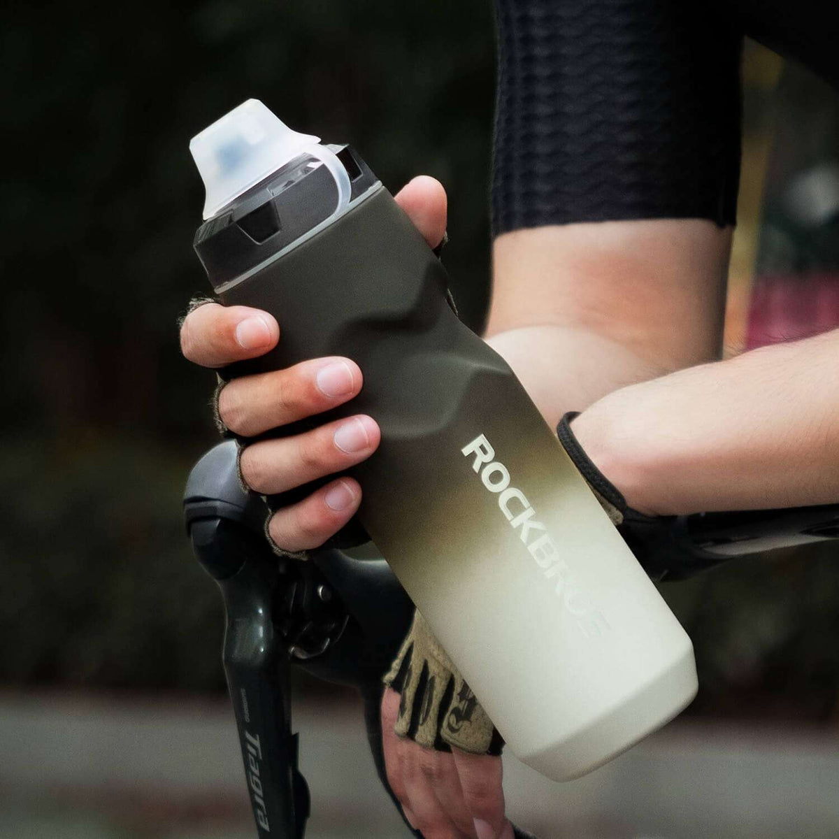Dark gray bike water bottle with flip-top lid, held by a cyclist