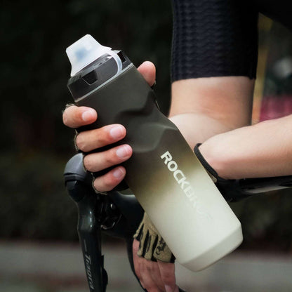 Dark gray bike water bottle with flip-top lid, held by a cyclist