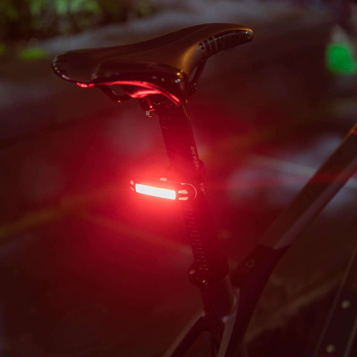 Close-up rear bike light glowing red at night with lens and mount visible