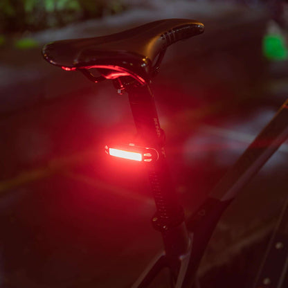 Close-up rear bike light glowing red at night with lens and mount visible