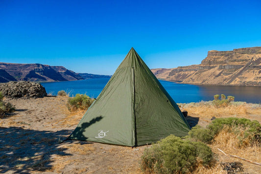 Green dome backpacking tent with rainfly pitched on sandy ground